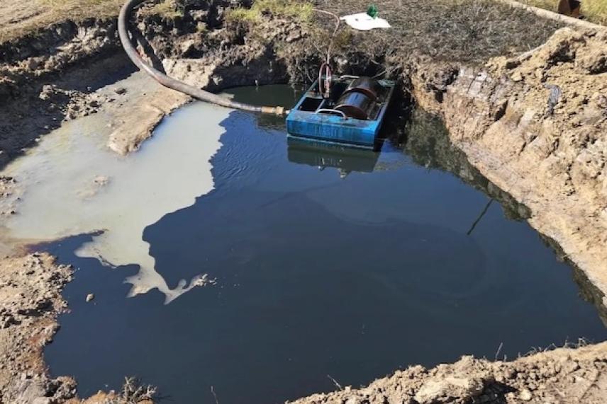 A large muddy pit with a blue container partially submerged.