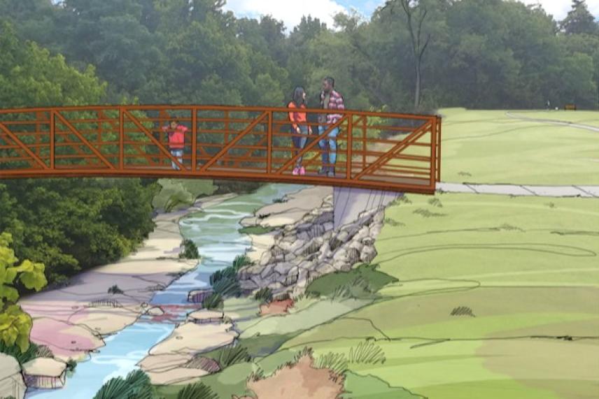 Red footbridge over a stream with people, surrounded by greenery.