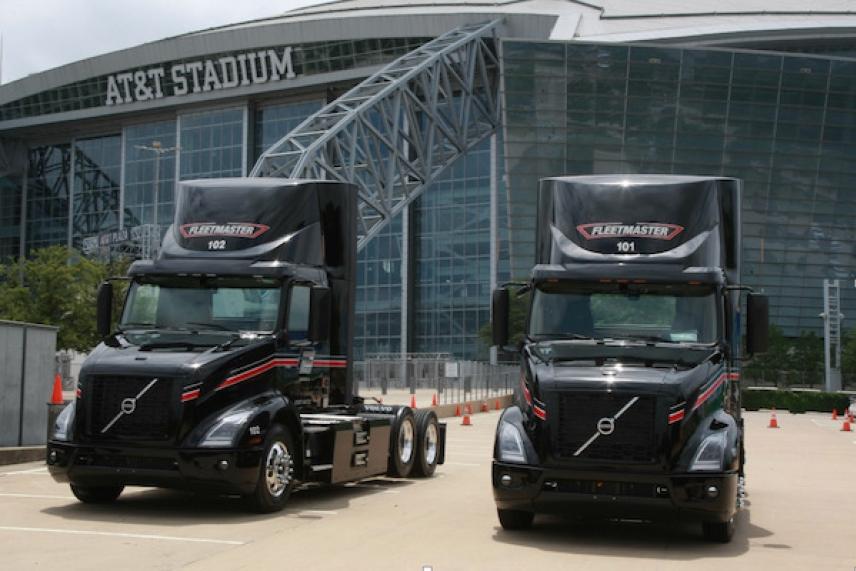 Two black trucks parked outside a large stadium.