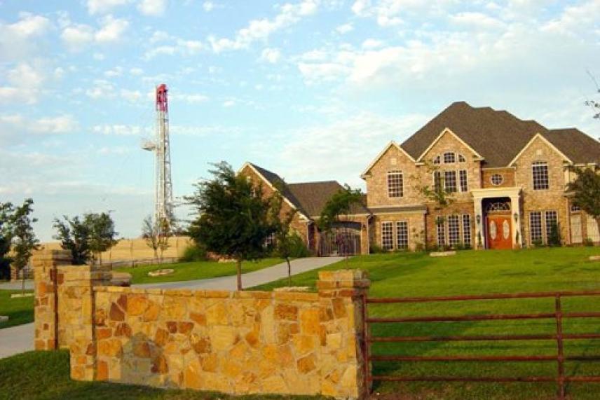 Large stone house with manicured lawn and an oil rig in the background.