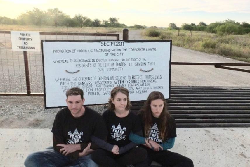 Three people sitting in front of a large sign on a rural road.