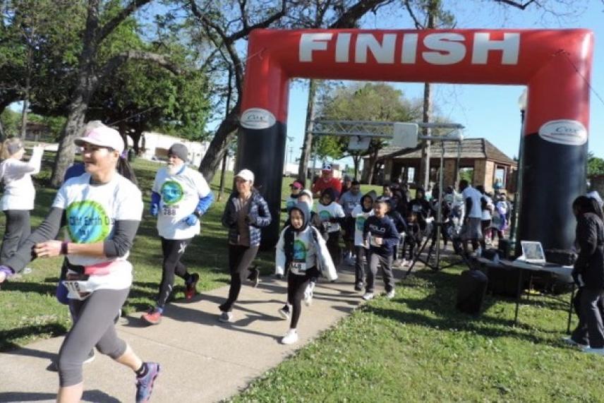 Runners crossing a finish line in a park.