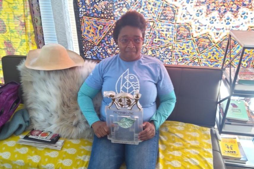 Woman in blue shirt holding an award, sitting on a decorated sofa.