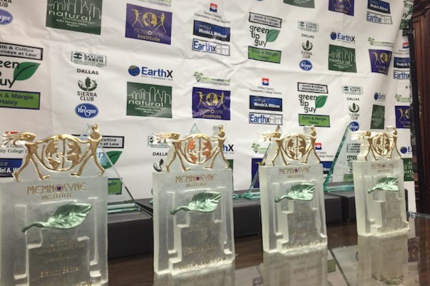 Four trophies with gold tops on a table, backdrop with logos.