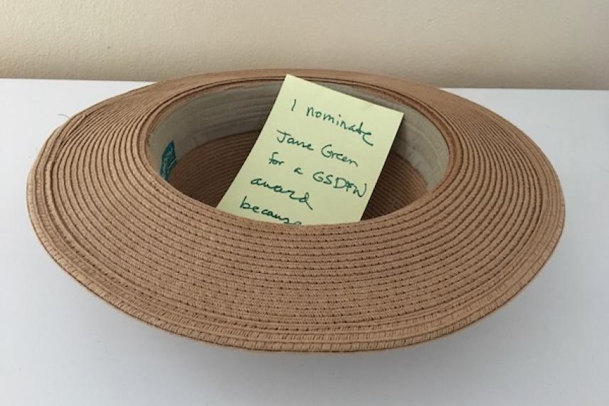 Brown straw hat on a white surface with a yellow note inside.