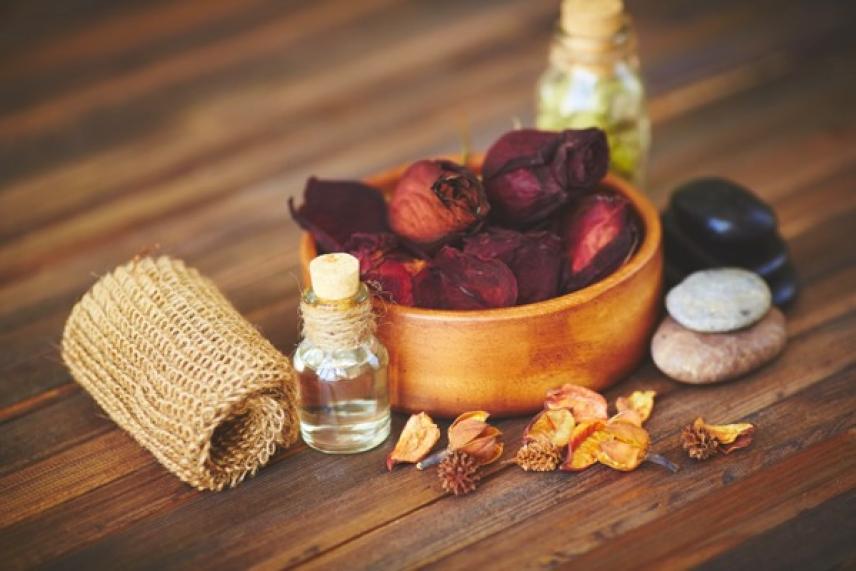 Potpourri in a wooden bowl, oils, stones, and a woven mat on a wooden surface.
