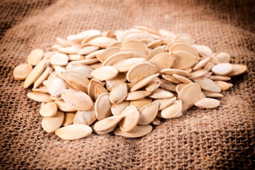 Pumpkin seeds scattered on burlap fabric.