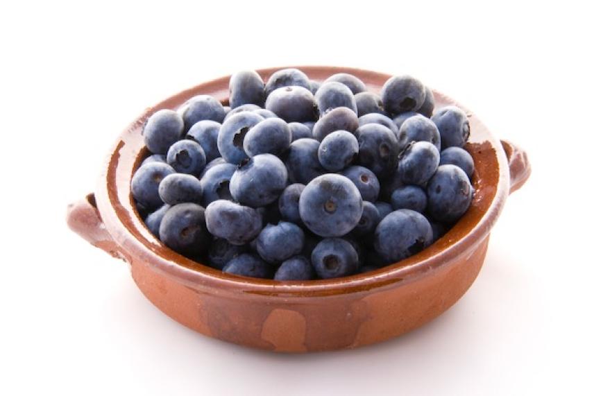Blueberries in a brown ceramic bowl on a white background.