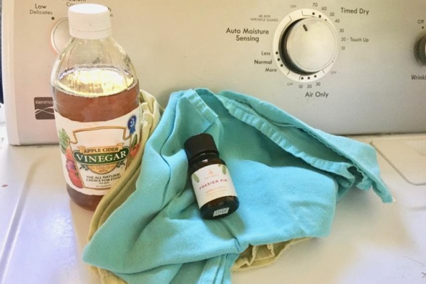Vinegar bottle, essential oil, and cloths on washing machine.