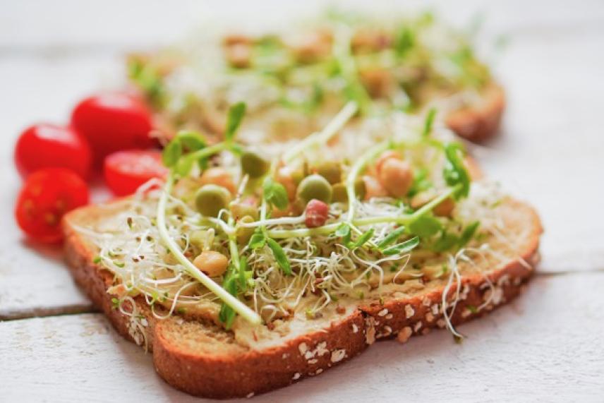 Toasted bread with sprouts and cherry tomatoes on a white surface.