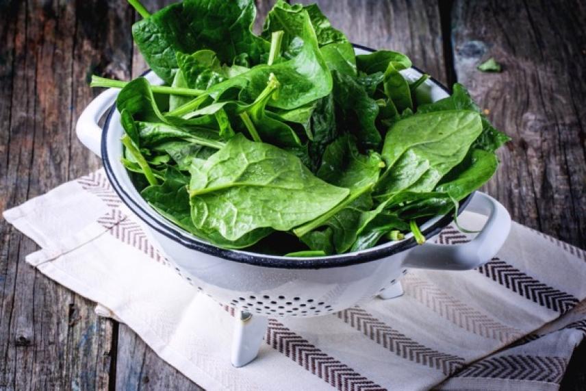 Fresh spinach leaves in a colander on a wooden surface.