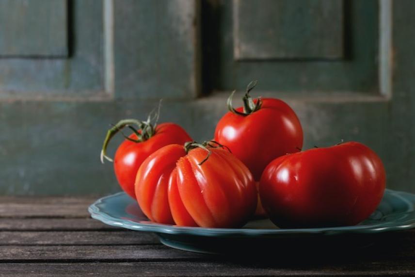 Four ripe tomatoes on a blue plate, wooden backdrop.