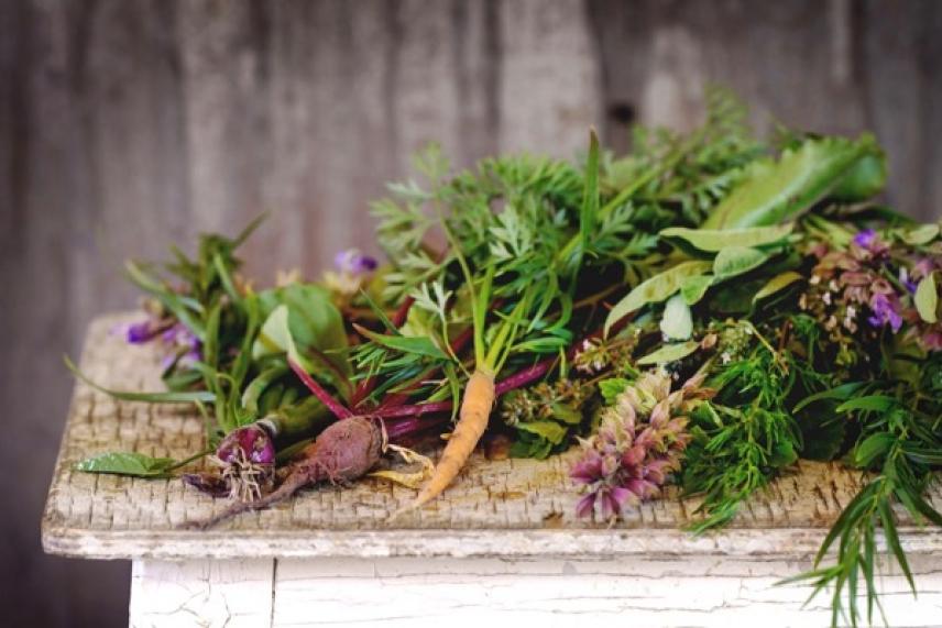 Fresh herbs and vegetables on a rustic wooden table.