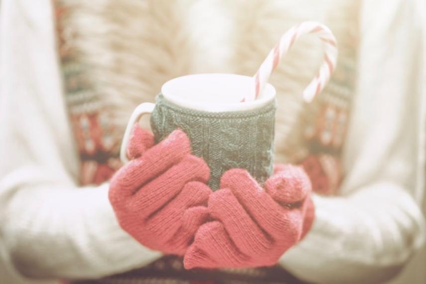 Cozy mug with candy cane, held with pink gloves.