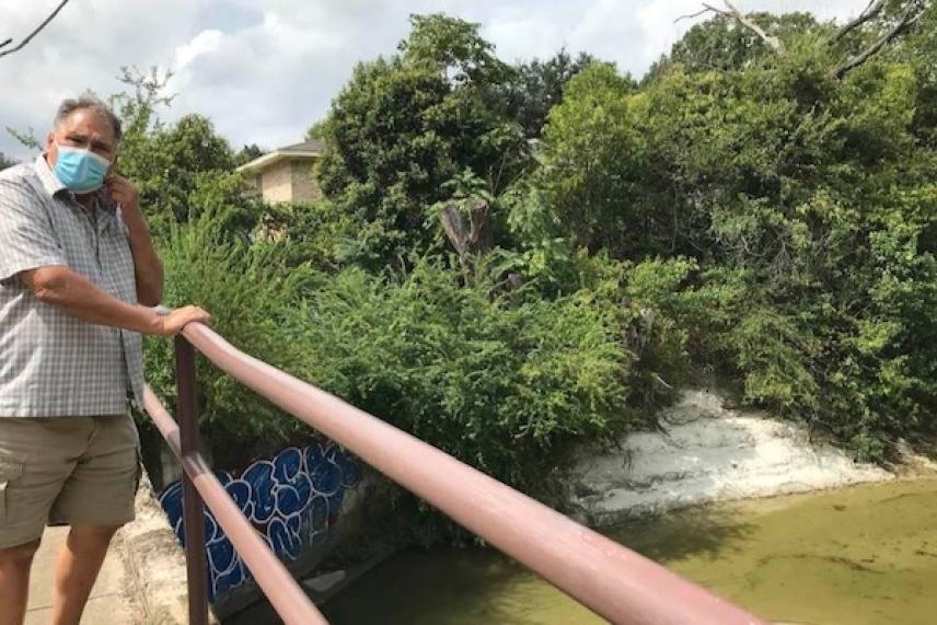 Man in mask on bridge over a small, tree-lined canal.