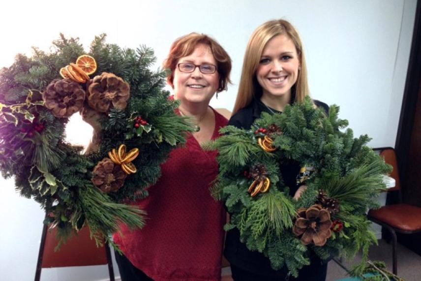 Two women smiling, holding decorated holiday wreaths.