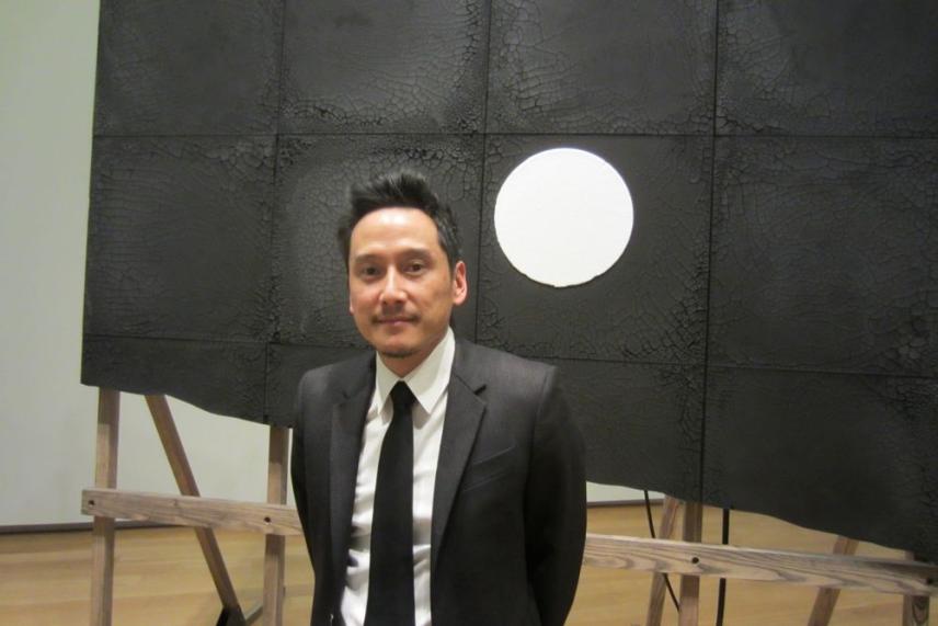 Man in a suit stands before a black artwork with a white circle.