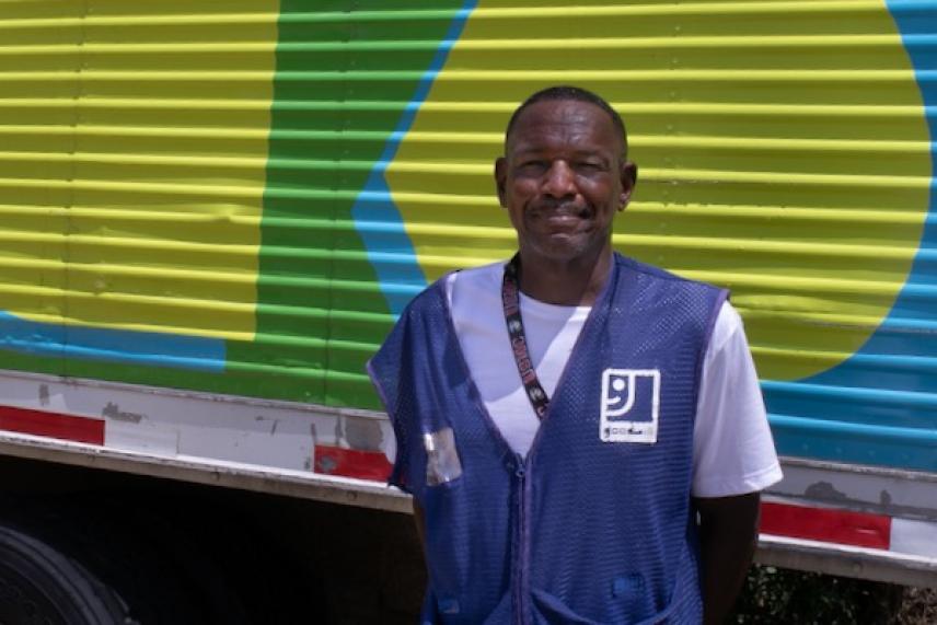 Man smiling in front of a colorful truck in a work uniform.
