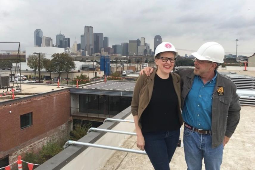 Two people wearing hard hats standing on a rooftop, city skyline in background.