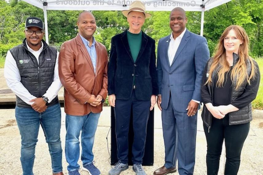 Five people smiling outdoors, standing under a tent on a sunny day.