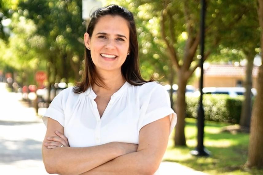 Smiling woman in white shirt standing on a sunny street with trees.