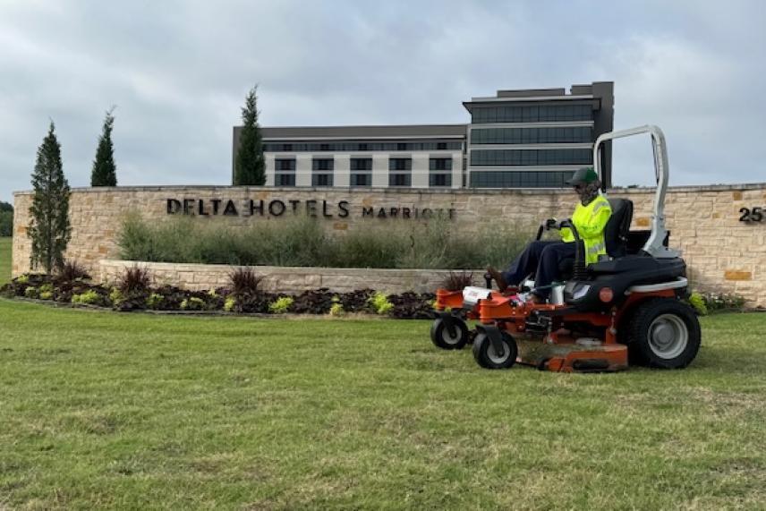 Worker mowing grass in front of Delta Hotels building.
