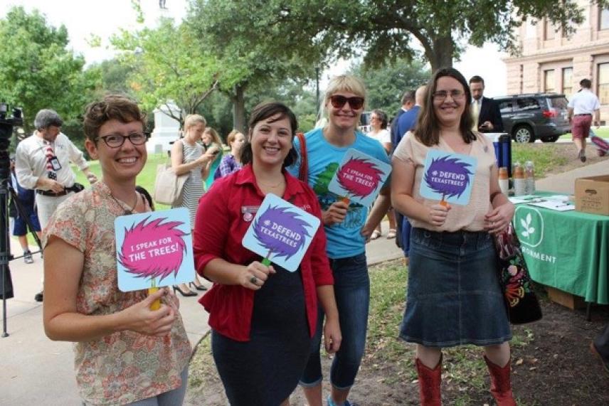Four smiling women holding colorful signs outdoors near a building.