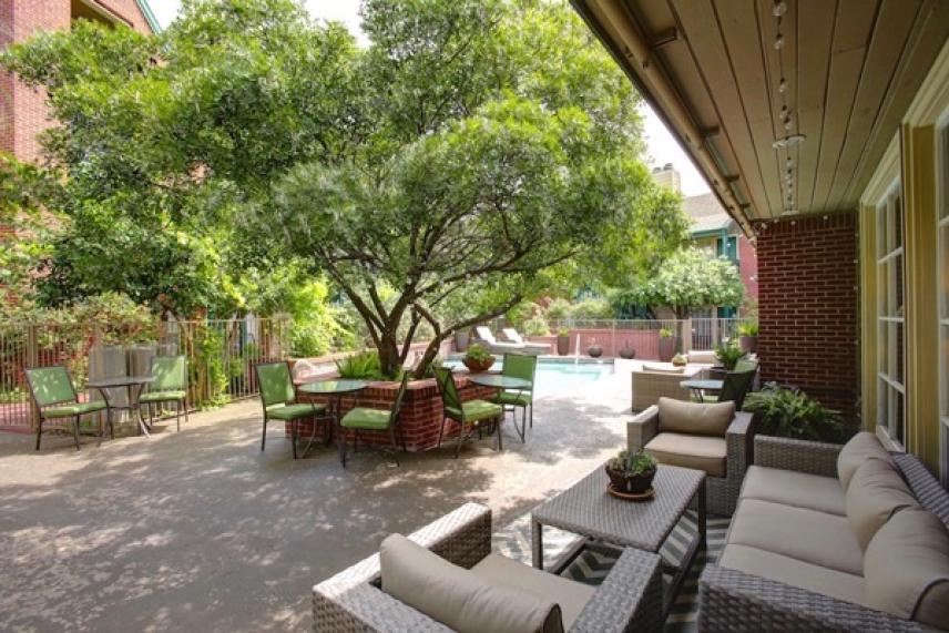 Courtyard with green trees, outdoor seating, and a pool in the background.