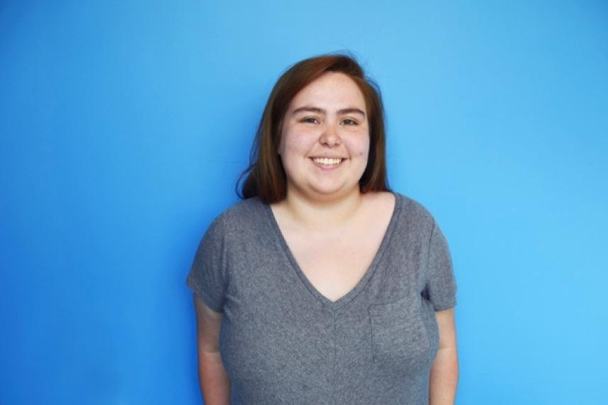 Smiling person in gray shirt against a blue background.