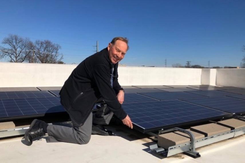 Man kneeling next to rooftop solar panels under clear blue sky.