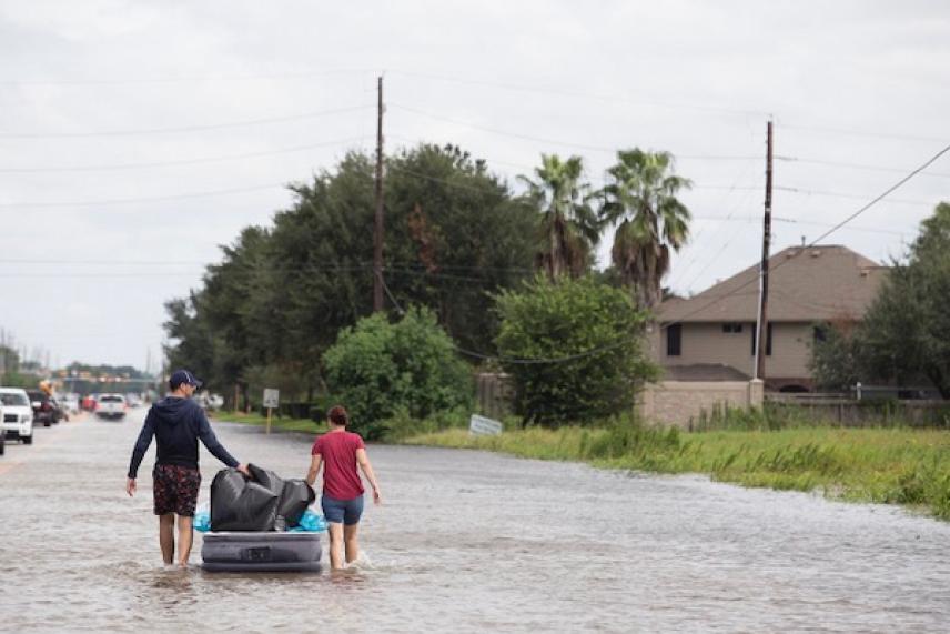 Two people pull a raft in a flooded suburban street.
