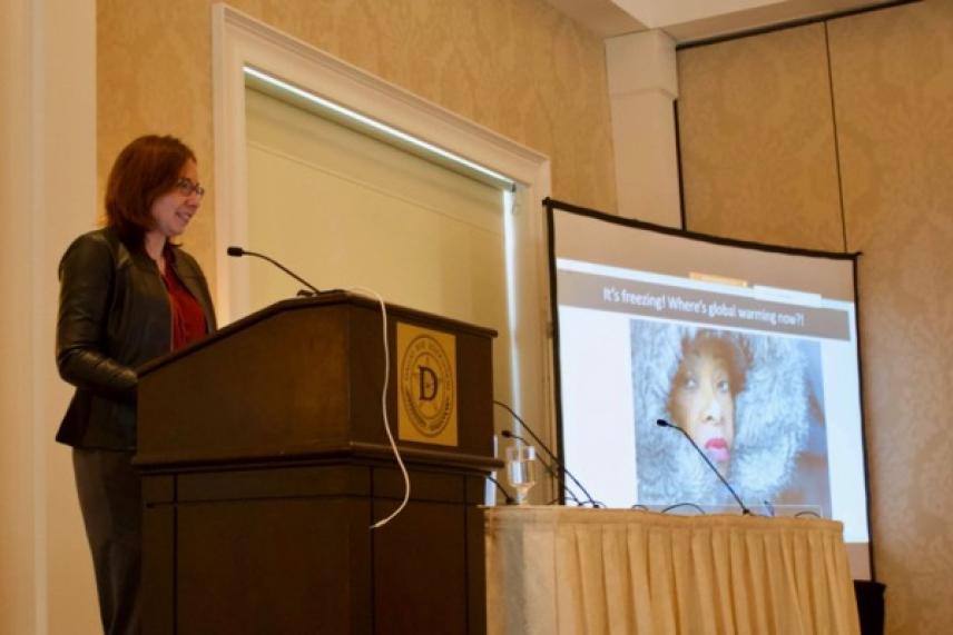 Speaker at a podium with a projection showing a close-up of a person wrapped in a scarf.