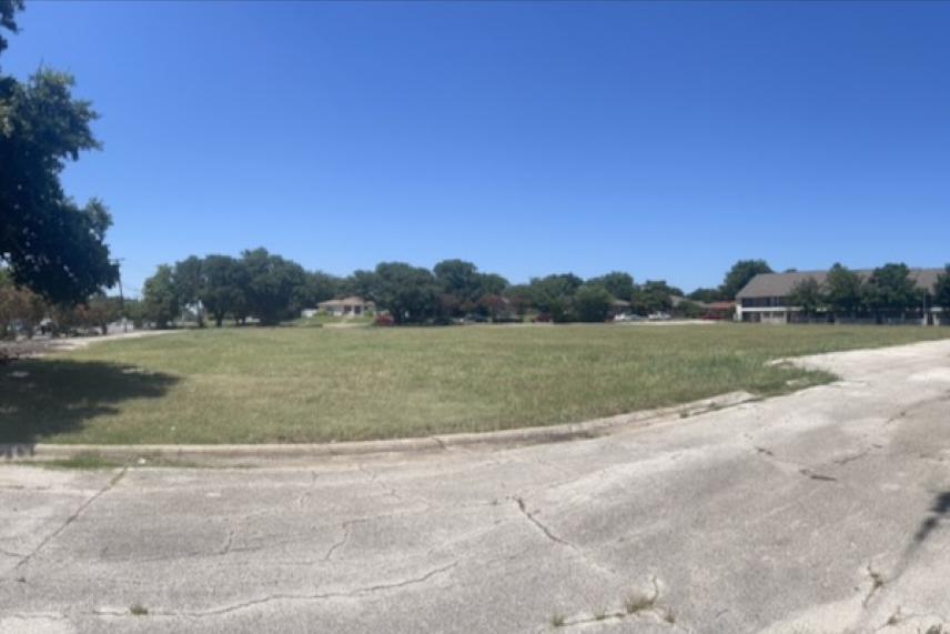 Open grassy field with trees in the background under a clear blue sky.