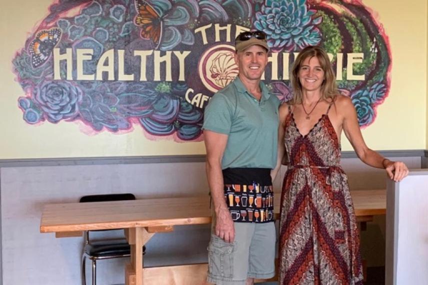 A man and woman smiling in front of a colorful café mural.