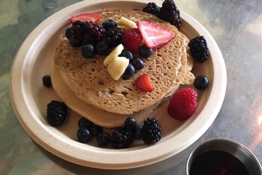 Pancakes topped with sliced bananas, strawberries, and mixed berries on a plate.