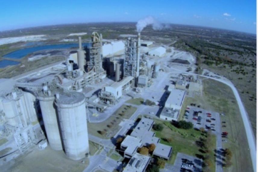 Aerial view of an industrial plant with smoke, surrounded by fields.
