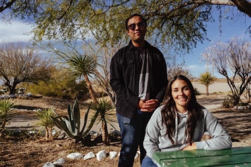 Man and woman outdoors, smiling near trees and desert plants.