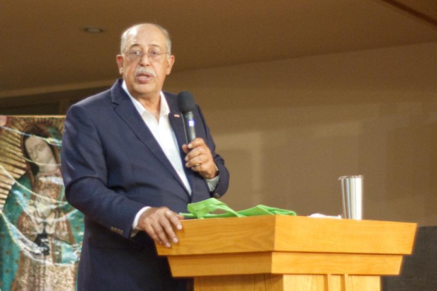 Man in a suit speaks at a podium, holding a microphone.