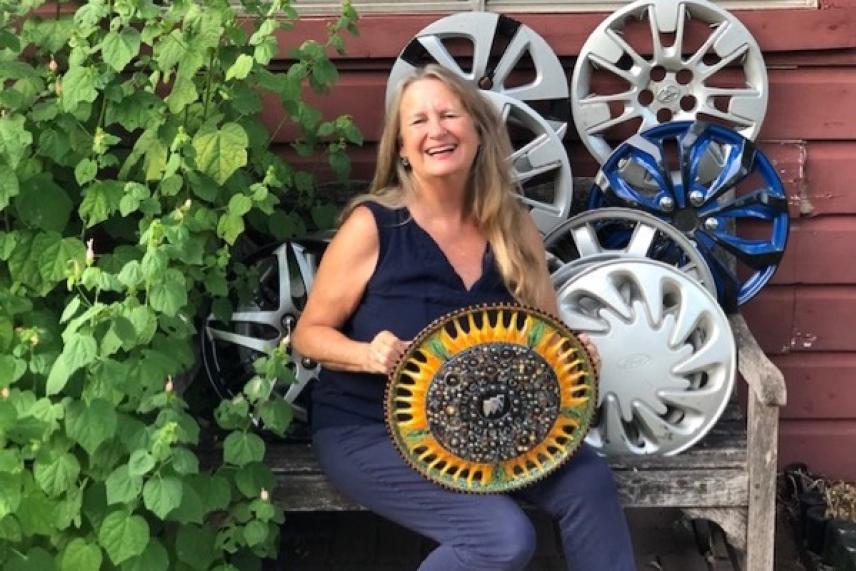 Smiling woman on bench with colorful wheel covers, green plants nearby.