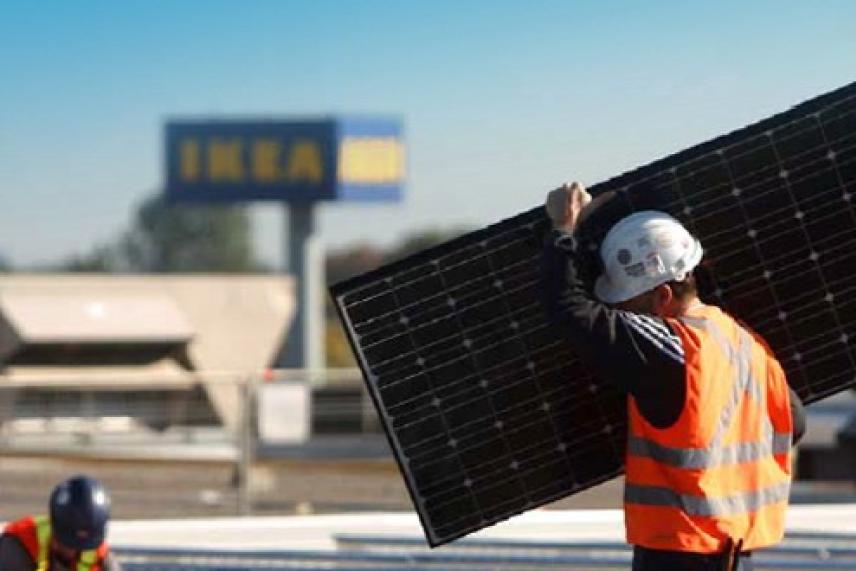 Worker in safety gear carrying solar panel near IKEA store.