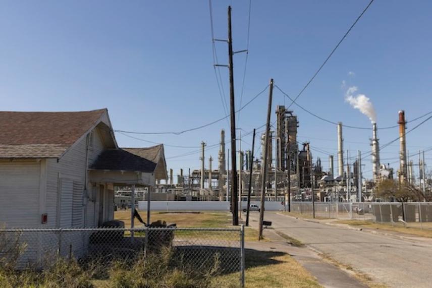 House near an industrial plant with smoke, clear sky.