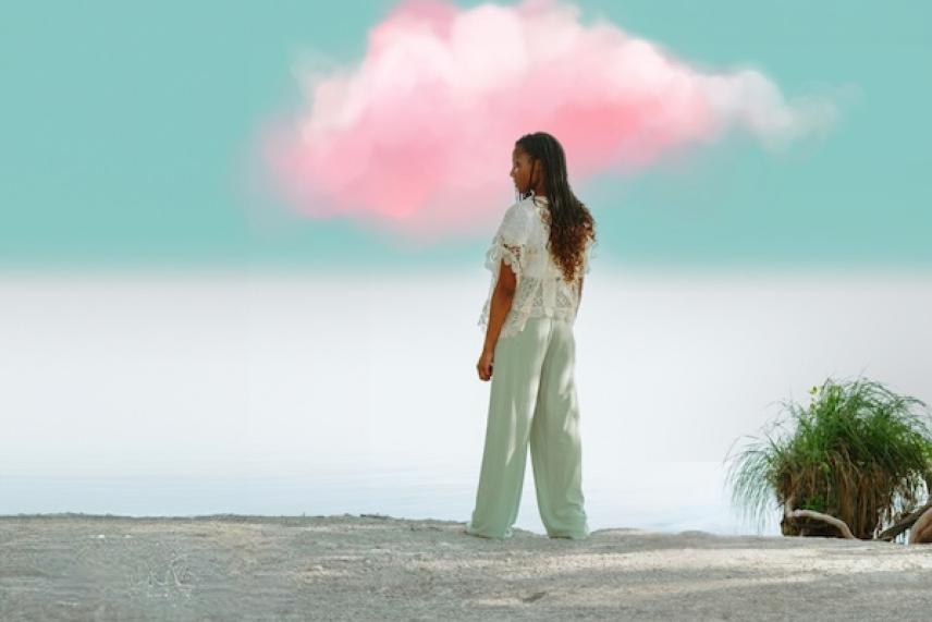 Woman standing by the sea under a pink cloud.