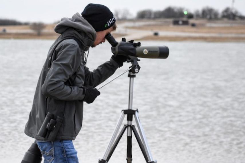 Someone observing through a spotting scope by a lake.