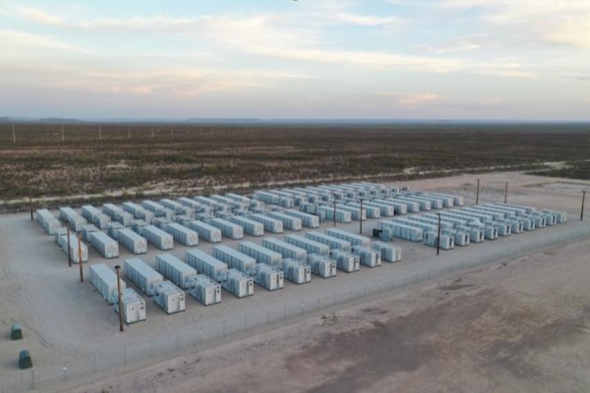 Battery storage facility with rows of white containers, set in a barren landscape under a cloudy sky.