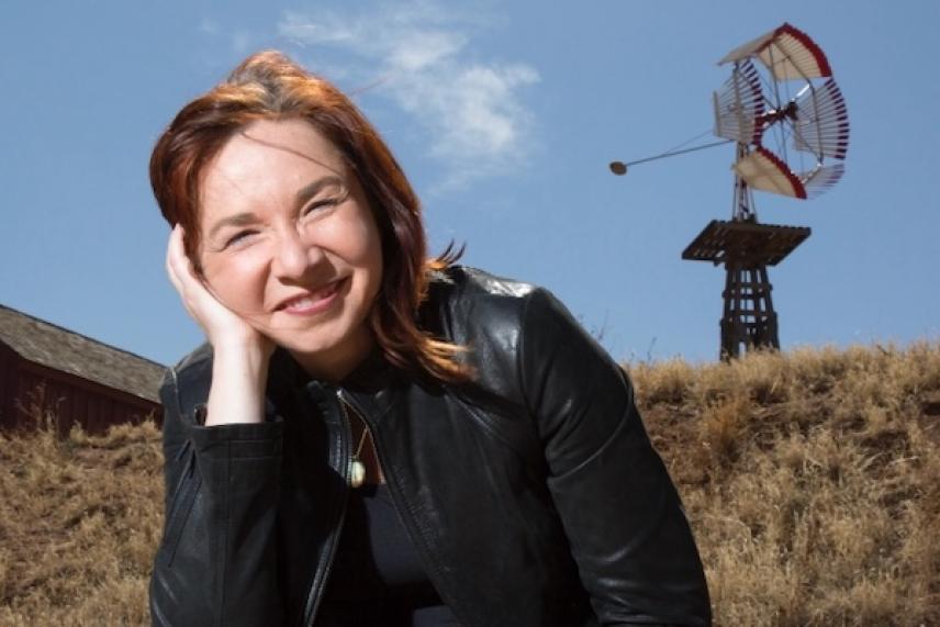 Smiling woman in black jacket outdoors, with windmill in the background.