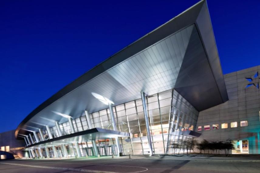 Modern building with angled roof and glass facade, lit up at night.
