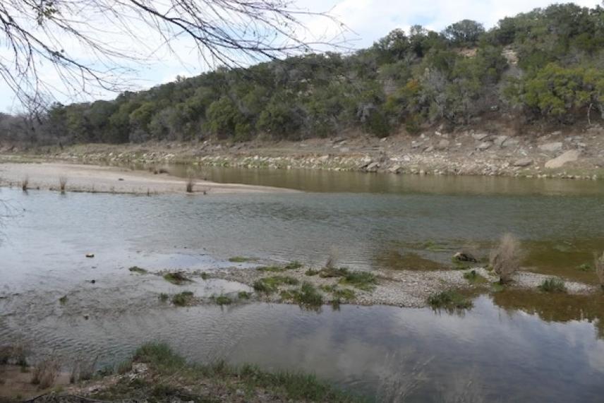 River with a rocky shore and trees in the background, under a cloudy sky.