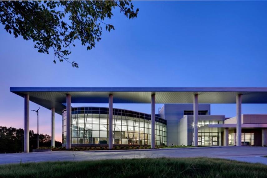 Modern building with glass facade at twilight, surrounded by trees.