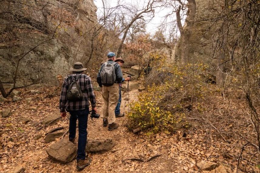 Three people hiking through a rocky, autumn forest trail.
