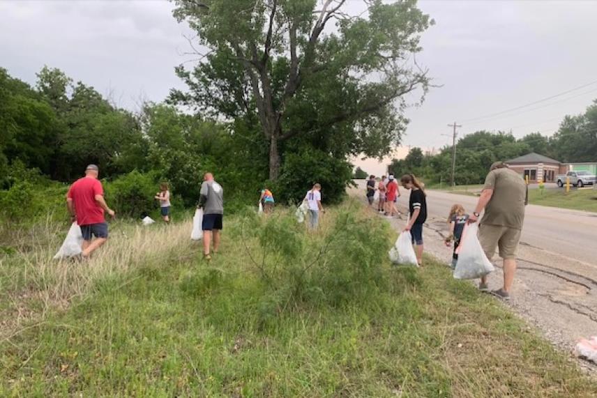 People collecting trash by a roadside under cloudy sky.